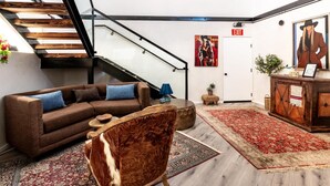 Un interior moderno con una escalera, un sofá de cuero marrón, una silla de madera y un tapete rojo estampado.