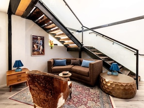 Uma sala de estar moderna com um sofá, uma mesa de centro de madeira, um tapete estampado, um cão e uma escada.