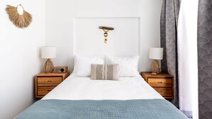 A bedroom with a bed, two bedside tables, a wall-mounted light fixture, and a patterned curtain. - Desert View Room w/ Fire Pit & Free Parking (Yucca Valley)