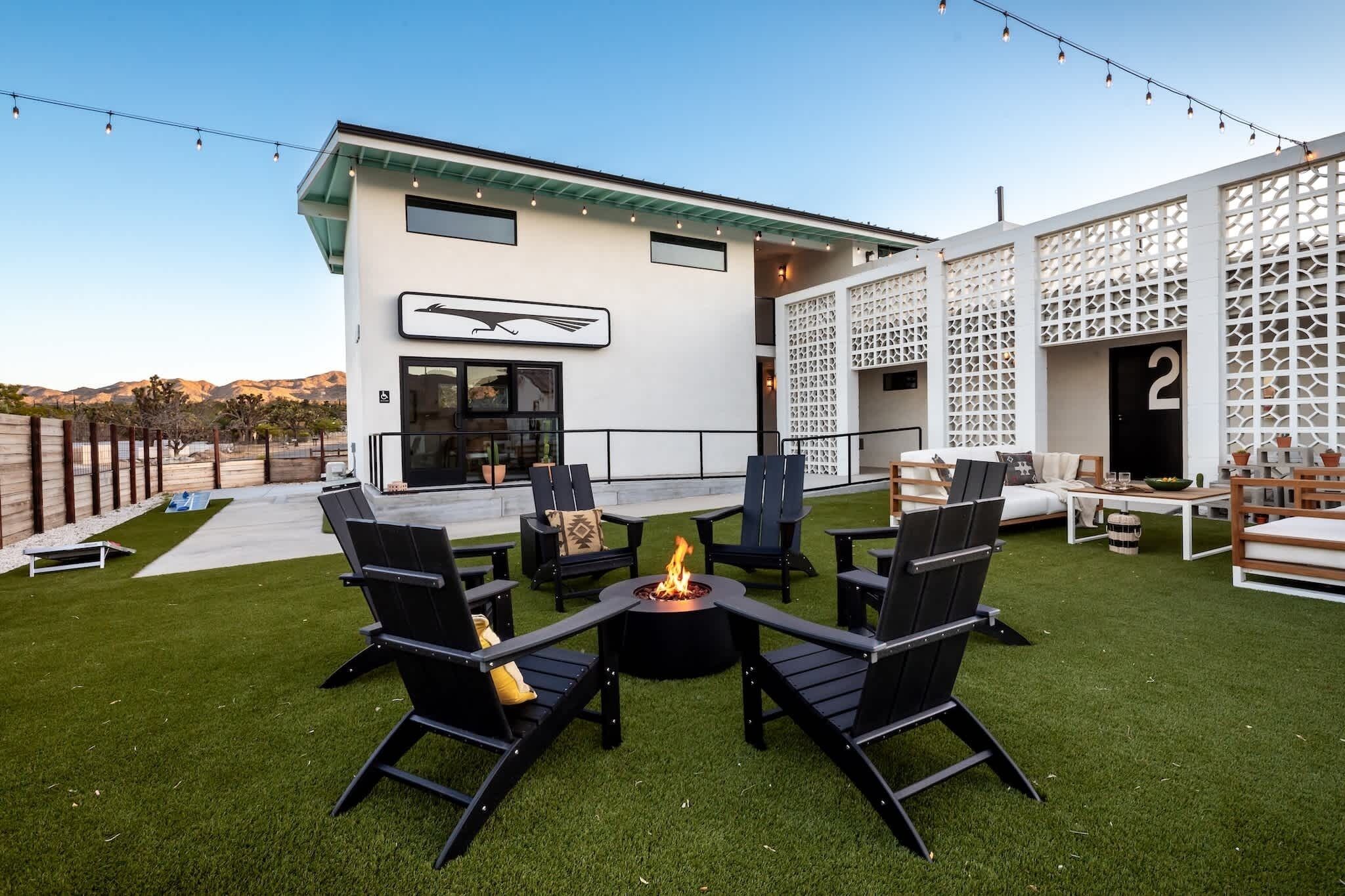 A modern outdoor patio with a fire pit, black chairs, and a white building with a number '2' sign.