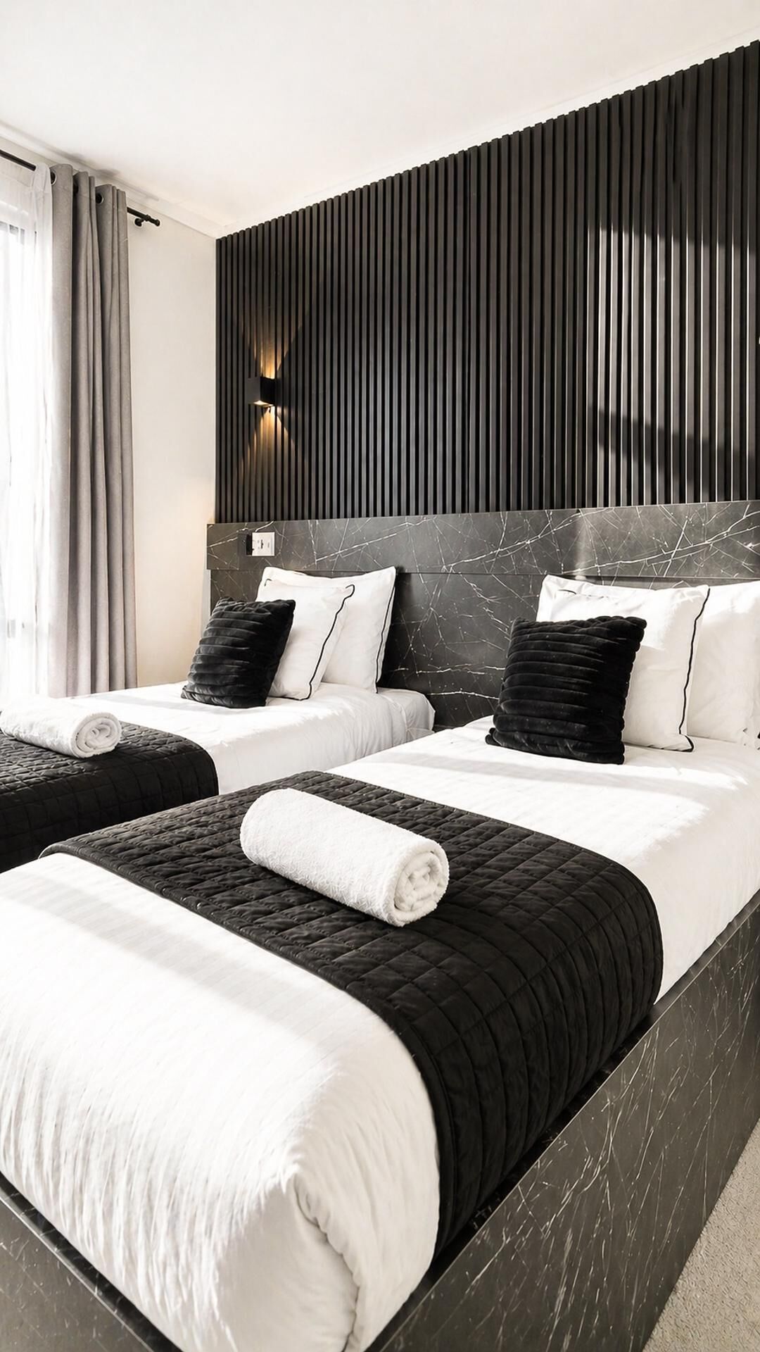 Habitación de hotel con dos camas, un cabecero oscuro y una lámpara moderna.