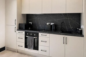 Uma cozinha moderna com painel de mármore preto, forno embutido e micro-ondas.