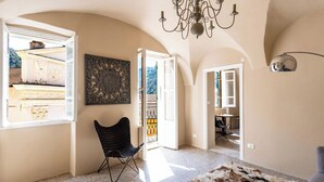 Ein Innenraum mit einer Chandelier, einem Sessel, einem Teppich und Blick durch eine geöffnete Tür.