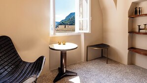 Ein Eckzimmer mit Fenster, einem kleinen Tisch, einem Stuhl und einem Regal.
