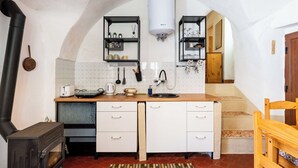 Una cucina compatta con stufa a legna, pensili bianchi e parete rivestita di piastrelle.