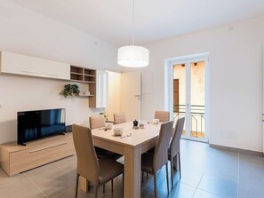 Ein moderner Essbereich mit Fernseher, Holztisch, Stühlen und einer Pendelleuchte.