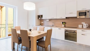 Une cuisine moderne avec des meubles blancs, un plan de travail en bois, un four encastré et un coin repas comprenant une table et des chaises.