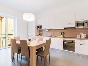 Eine moderne Küche mit weißen Schränken, einer Holzausziehtafel, einem eingebauten Backofen und einem Essbereich mit Tisch und Stühlen.