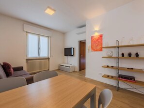 Ein modernes Wohnzimmer mit einem Holzesstisch, einer Couch, einem Fernseher und einem Bücherregal mit Dekoration.