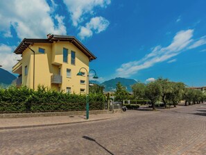 Ein gelbes Gebäude mit Balkon, Pflasterstraße und Bäumen.