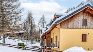 A wooden chalet with a balcony, surrounded by snow-covered trees and a wooden fence. - Cosy apartment for 4 people with WIFI, TV and balcony (Varzo)
