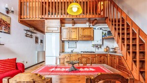 A kitchen with wooden cabinets, a dining table with a red tablecloth, and a staircase. - Cosy apartment for 4 people with WIFI, TV and balcony (Varzo)