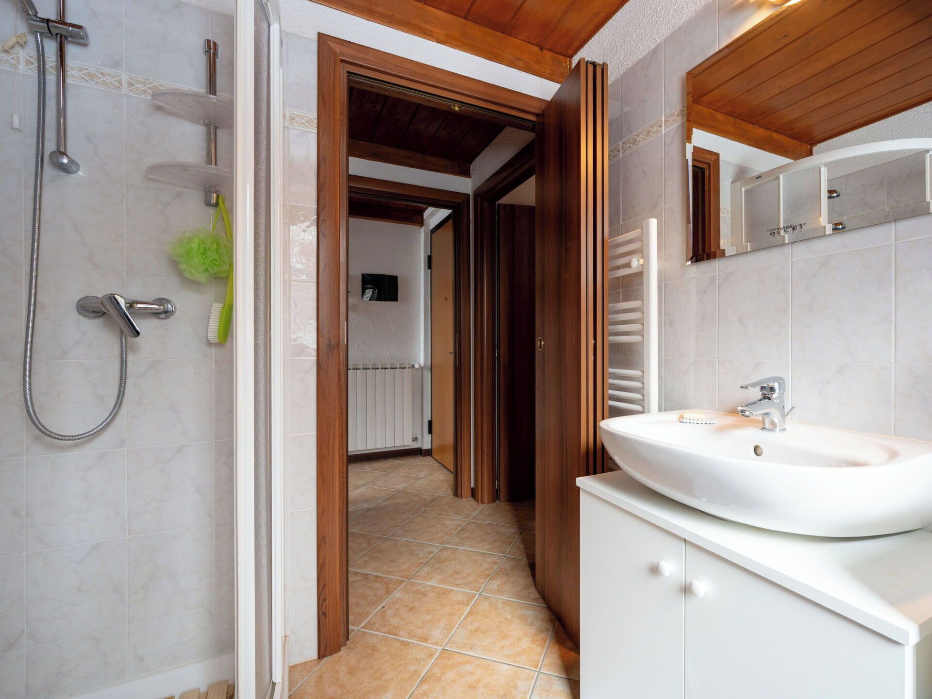 Une salle de bain avec une douche, un lavabo et une porte en bois donnant sur un couloir.