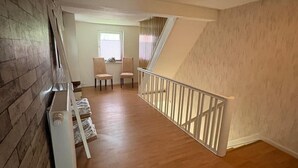 A spacious hallway with wooden flooring, a staircase, and a dining area with chairs and a table.