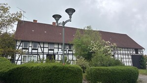 A traditional half-timbered building with a tiled roof, a street lamp, and well-maintained hedges.