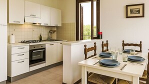 Cocina compacta con comedor, que incluye armarios, estufa y una mesa dispuesta para cuatro.