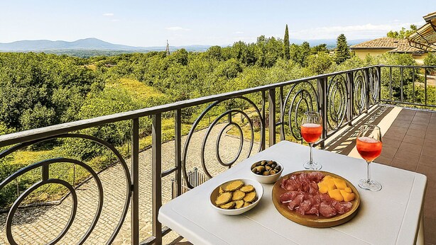 Un balcón con una mesa preparada para una comida, vistas a un viñedo y una cadena montañosa al fondo.