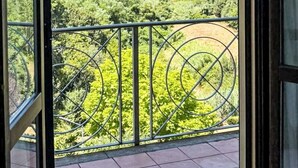 Un balcón con baranda de metal, vistas despejadas de un paisaje verde con árboles y una montaña a lo lejos.