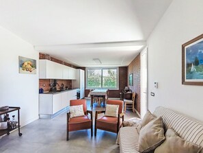 Eine moderne Küche mit weißen Schränken, eine Essecke mit Tisch und Stühlen sowie ein Wohnzimmer mit Sofa und Gemälde.
