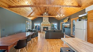 A spacious room with a long wooden table, comfortable seating, a stone fireplace, and a view of the outdoors.
