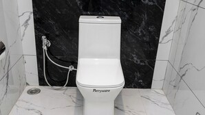 Un inodoro blanco con etiqueta Parryware, un bidé portátil y una pared de mármol negro.