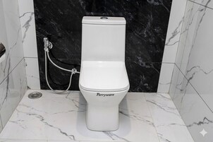 A white toilet with a Parryware label, a handheld bidet, and a black marble wall.