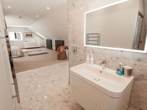 A modern bathroom with a large mirror, a white sink, and toiletries. - Midways (Windermere)