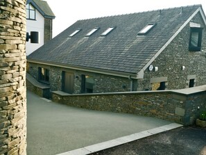 A stone building with a sloped roof, skylights, and a paved driveway. - Midways (Windermere)