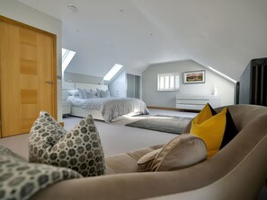 A modern bedroom with a sloped ceiling, a large bed, a sofa, and a side table. - Midways (Windermere)