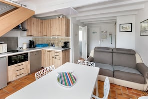 Eine kleine Küche mit modernen Geräten, ein Essbereich mit weißem Tisch und ein graues Sofa.