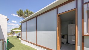 A modern building with a large sliding door, a small kitchen with a refrigerator, and a grassy area with a white fence. - Apartment 'El Encanto' with Mountain View, Private Pool and Wi-Fi (Villarrasa)