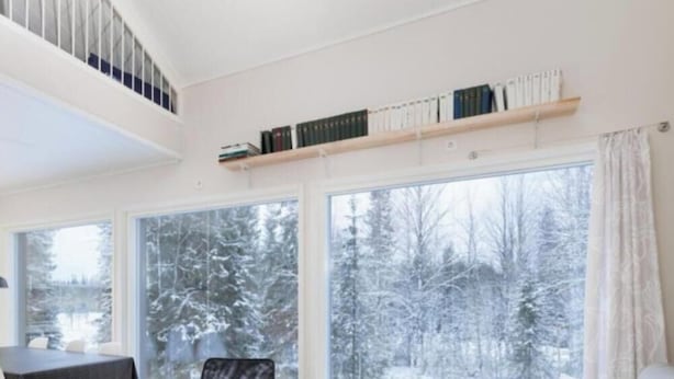 Quarto com amplas janelas, uma estante de livros e vista para uma floresta nevada.
