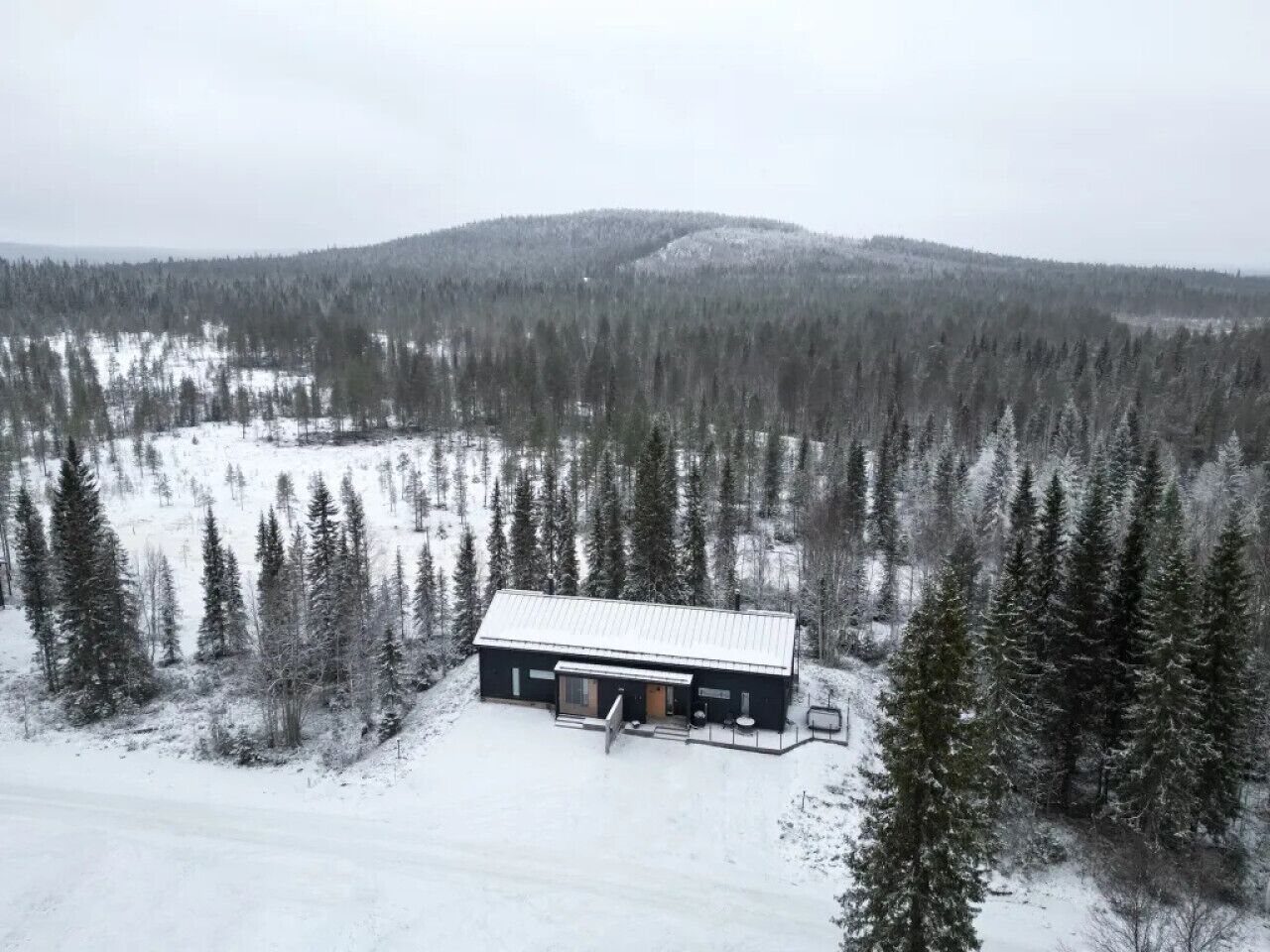 En hytte med metal tag, omgivet af skov og et sneklædt landskab.