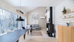 Um interior moderno com área de jantar, sofá, lareira e vista para árvores cobertas de neve.