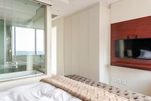 Ein Schlafzimmer mit Bett, Fenster, Wandfernseher und Ausblick nach draußen.
