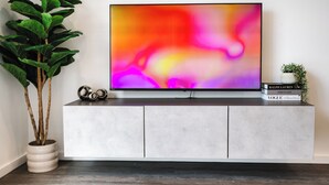 A flat-screen TV mounted on a white cabinet with a plant and books beside it. - 1 Bed City Centre Apt | Sleeps 4 | Juliet Balconies | Long Term Stays Available (Salford)