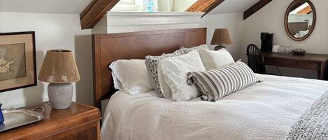 A bedroom with a wooden ceiling, a bed with white bedding, a bedside table with a lamp, and a floral-patterned rug.