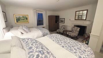A hotel room with two beds, a fireplace, a painting, and a window with curtains.