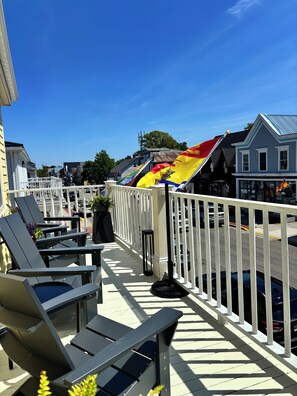 A balcony with outdoor seating, a railing, and a storefront with a sign.