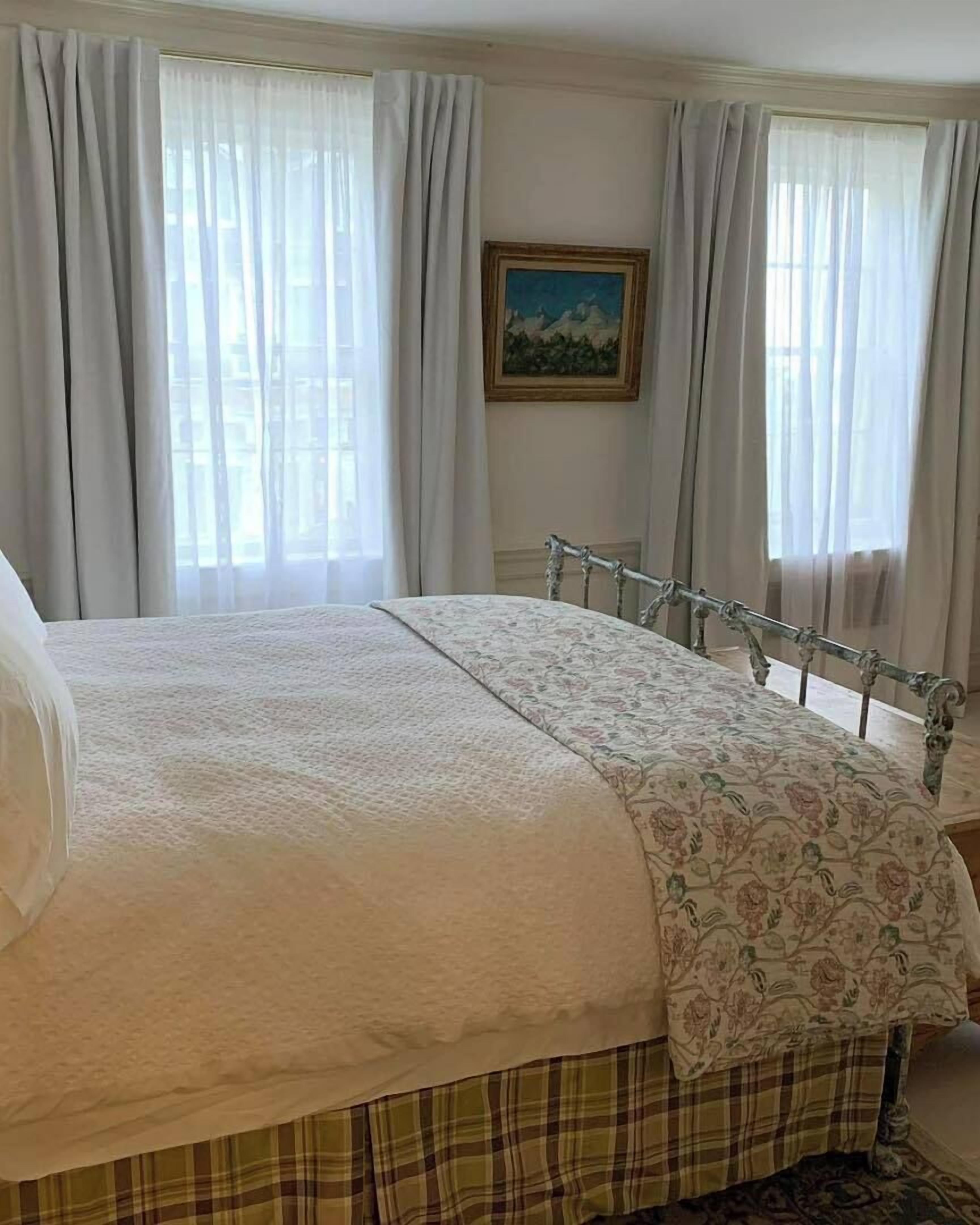 Un dormitorio con cama, cortinas, un cuadro y una ventana.