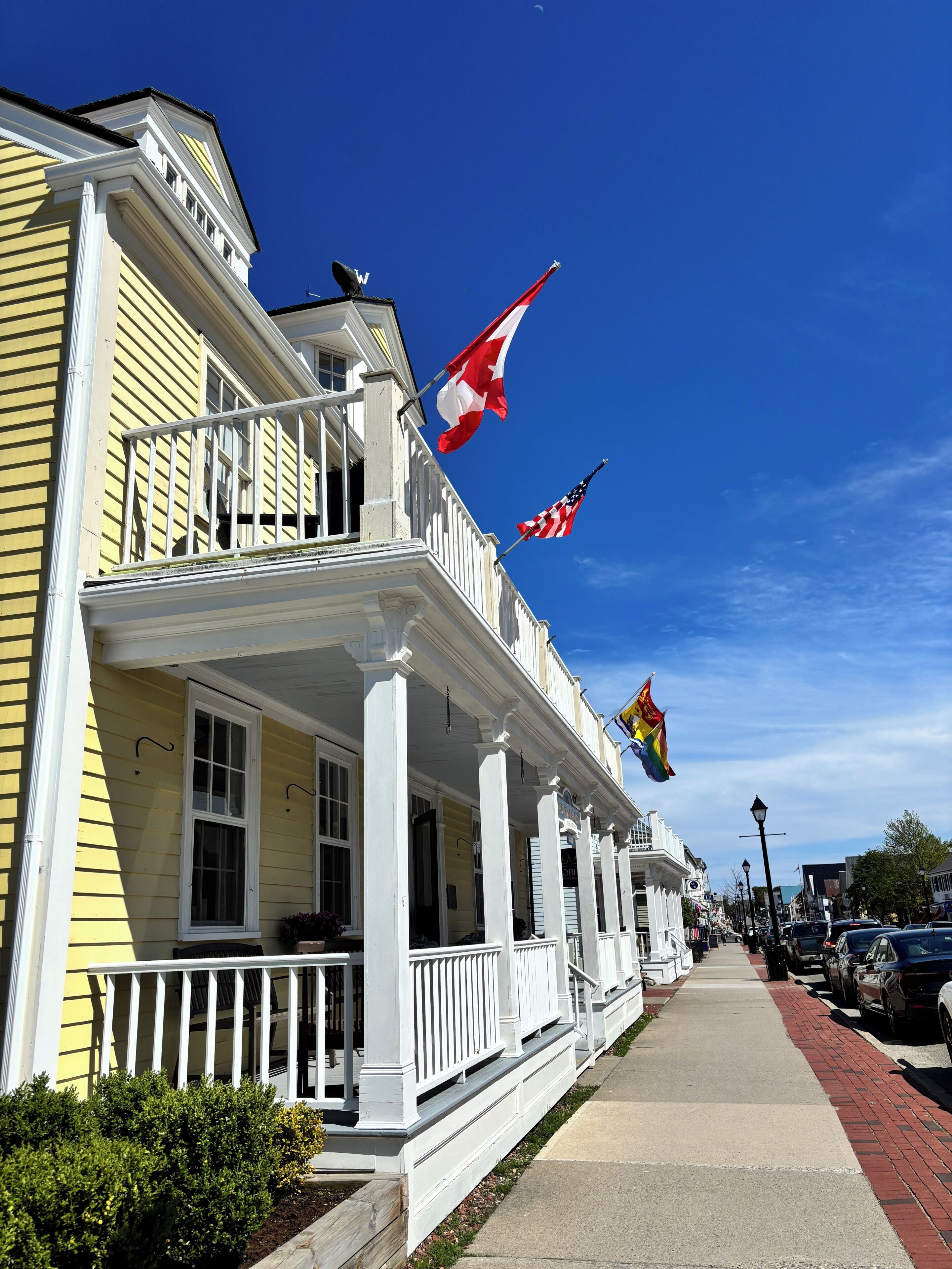 Un edificio amarillo con detalles blancos, un balcón y varias banderas, incluyendo las de Canadá y Estados Unidos.