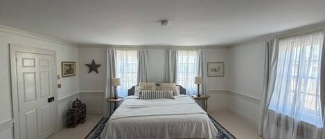 A bedroom with a large bed, two bedside tables, a radiator, and a window with curtains.