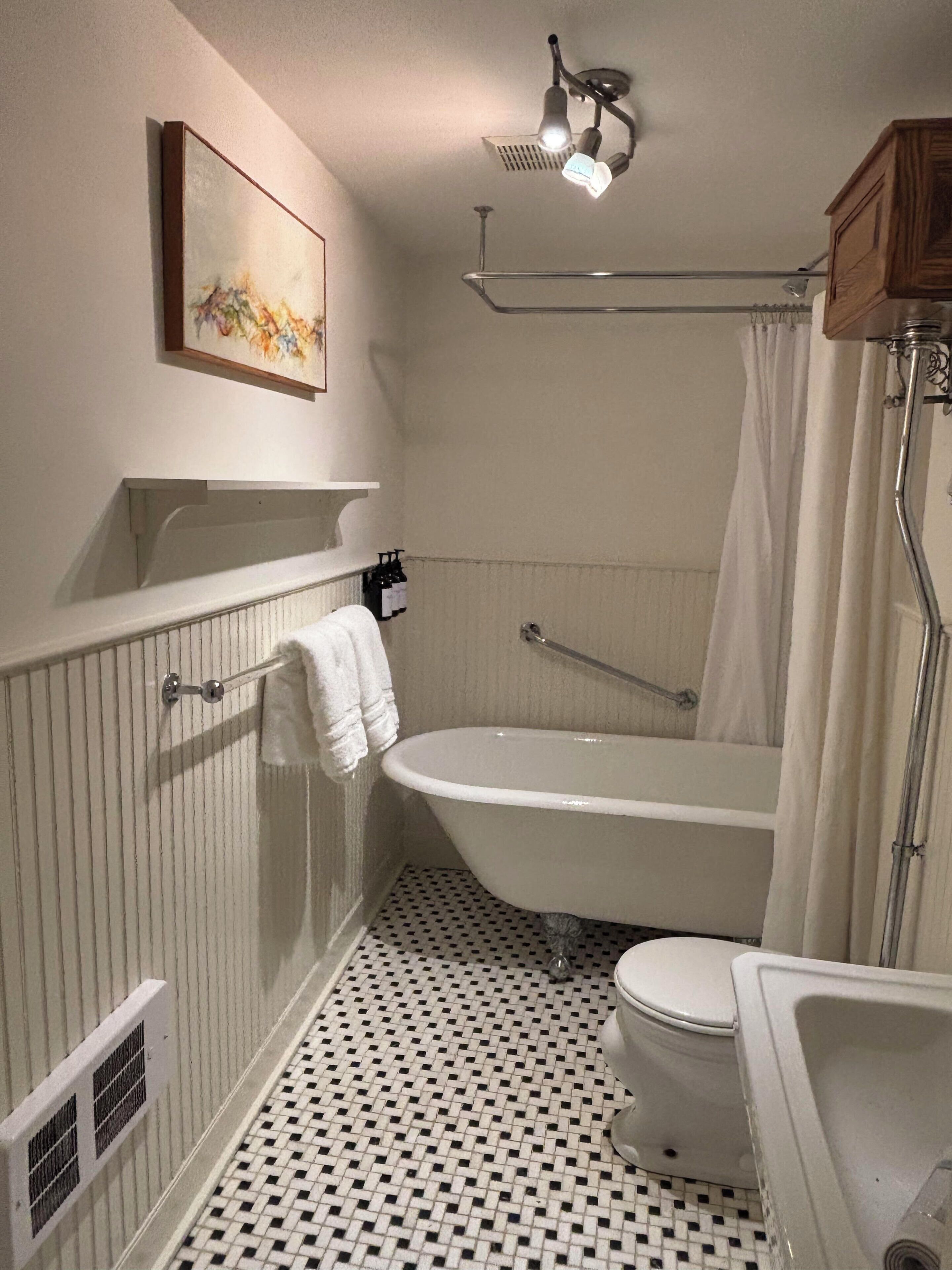A bathroom with a freestanding bathtub, a toilet, a sink, and a shower curtain.