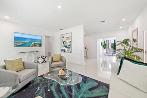 Ein modernes Wohnzimmer mit einer Couch, Sesseln, einem Glastisch und Kunstwerken an den Wänden.