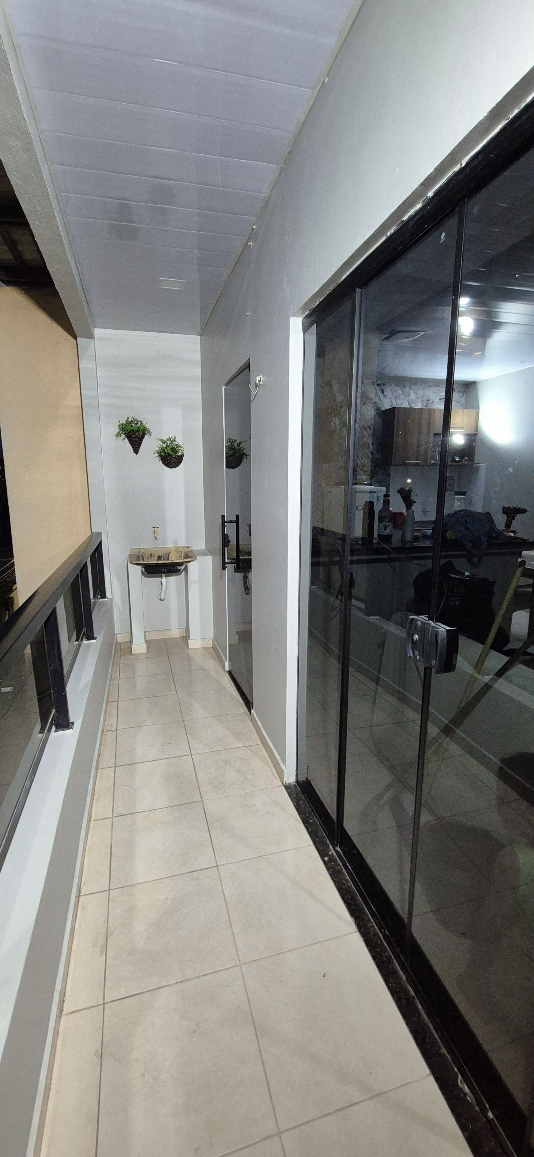 Um corredor com pia, plantas penduradas e uma porta de vidro que dá para uma cozinha.