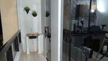 Um corredor com pia, plantas penduradas e uma porta de vidro que dá para uma cozinha.