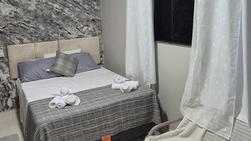 A bedroom with a bed, a smaller bed, a window with curtains, a marble wall, and a ceiling light.