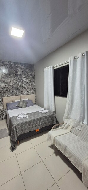 Ein Schlafzimmer mit einem Bett, einem zusätzlichen Bett, einem Fenster mit Vorhängen, einer Marmorwand und einer Deckenleuchte.