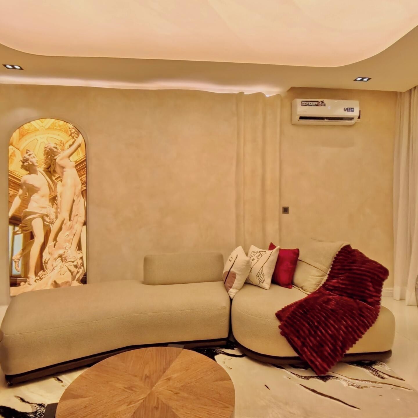 A modern living room with a beige sofa, a red throw blanket, and a unique wall-mounted sculpture.
