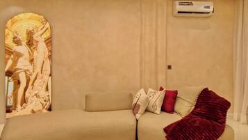 A modern living room with a beige sofa, a red throw blanket, and a unique wall-mounted sculpture.